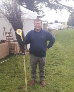 Man standing with besom broom the broom has a prize ribon atached to it
